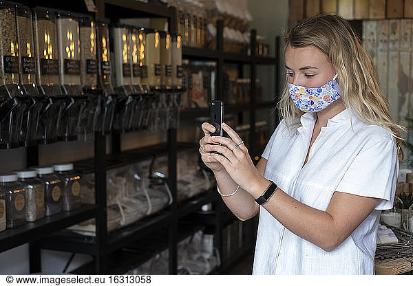 Woman wearing face mask in waste-free local store  using a mobile phone