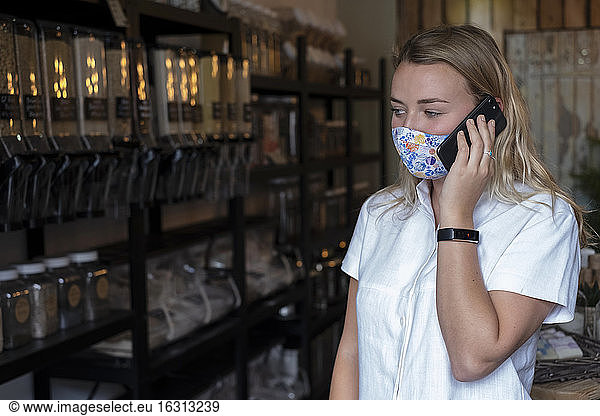 Woman wearing face mask in waste-free local store  using a mobile phone