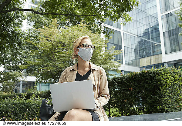 Woman wearing face mask using laptop while sitting at office park in city