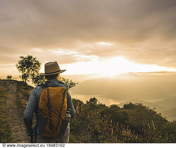 Woman wearing hat hiking on mountain at sunset