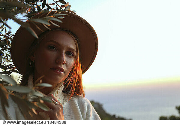 Woman wearing hat near olive tree at sunset