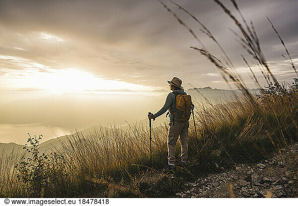 Woman wearing hat standing with hiking poles at sunset