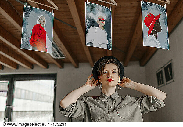 Woman wearing hat while standing under painted image hanging in studio
