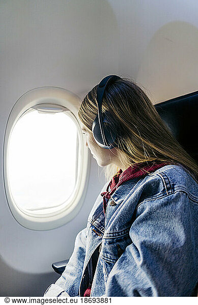 Woman wearing headphones looking out of window sitting in airplane