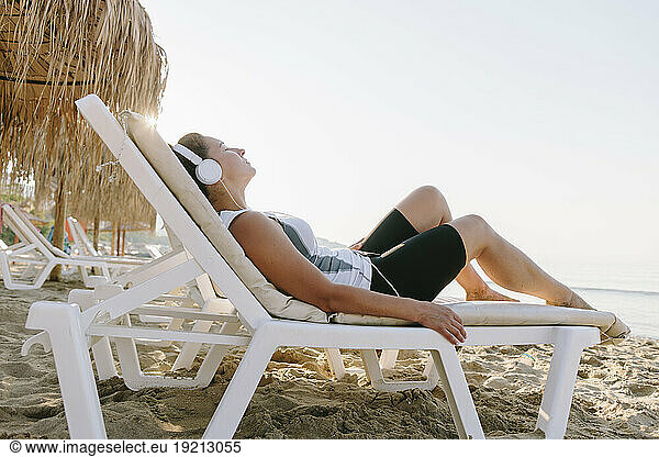 Woman wearing headphones relaxing on lounge chair at beach