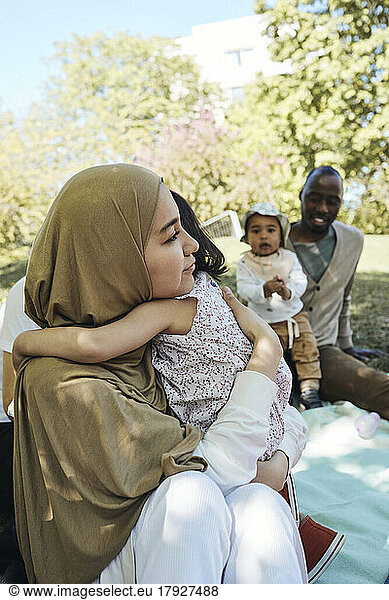 Woman wearing headscarf embracing daughter at park