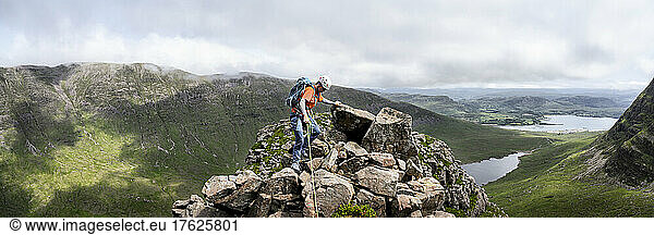 Woman wearing helmet climbing on top of rocky mountain