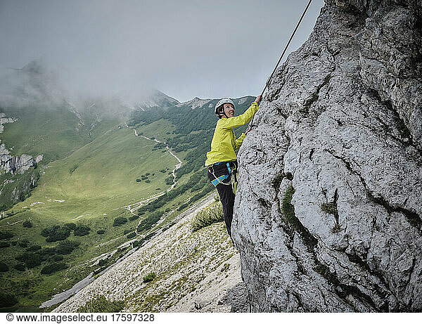 Woman wearing helmet climbing rocky mountain