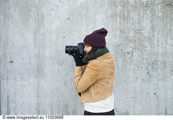 Woman wearing jacket photographing against wall