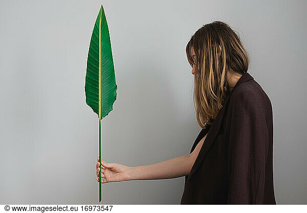 Woman wearing jacket posing with a green palm leaf.