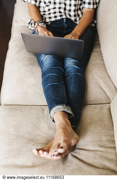 Woman wearing jeans lying on a sofa  using a laptop computer.