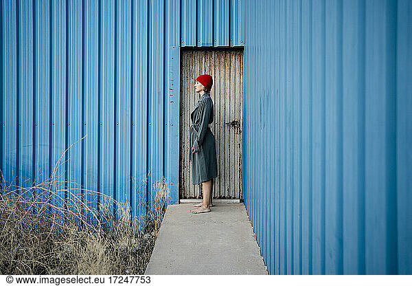 Woman wearing knit hat standing by corrugated iron door