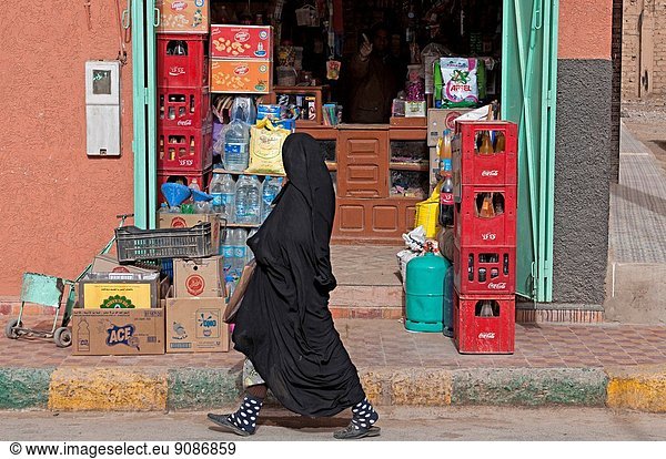 Woman wearing moroccan niqab walking by a shop on the streets of Rissani  Ziz Valley  Morocco.