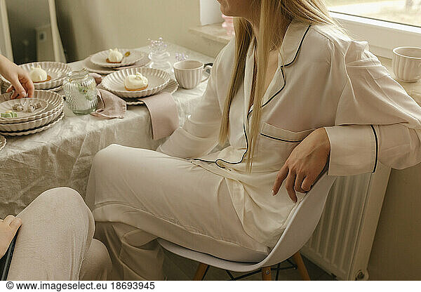 Woman wearing pajamas sitting on chair at dining table at home