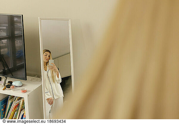 Woman wearing pajamas taking mirror selfie standing at home