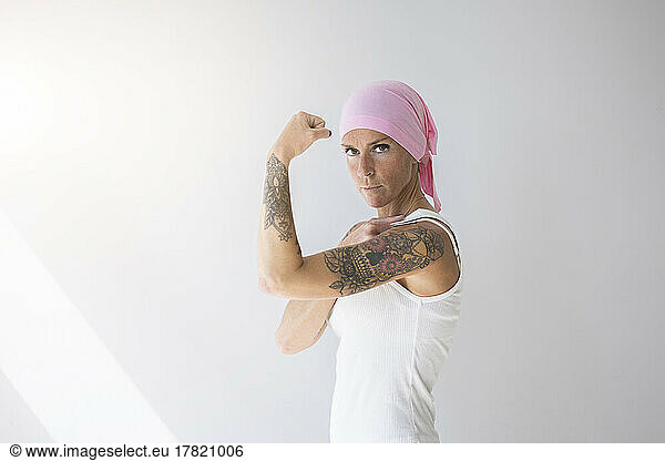Woman wearing pink scarf flexing muscles in front of wall