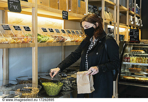 Woman wearing protective face mask buying green peas at supermarket during pandemic