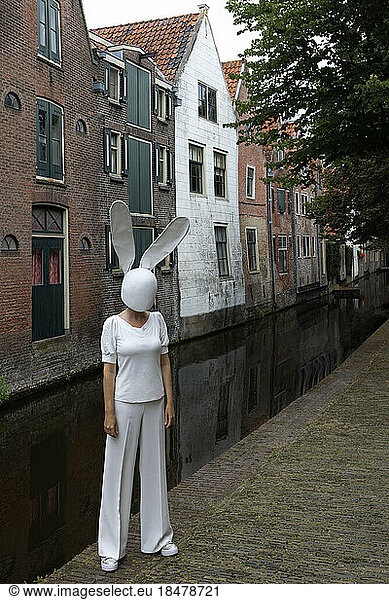 Woman wearing rabbit mask standing on footpath