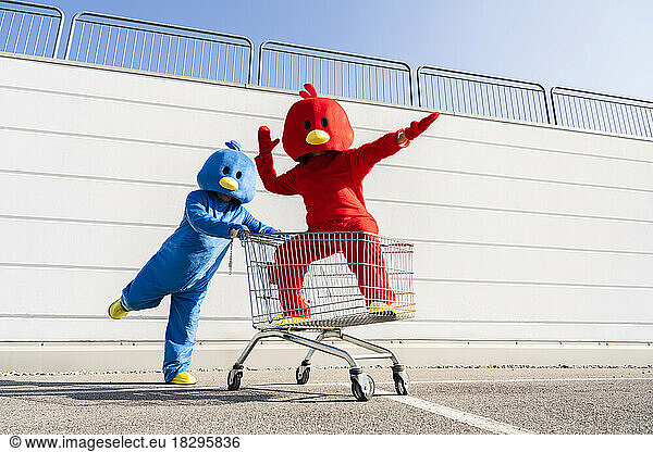 Woman wearing red duck costume having fun with man pushing shopping cart