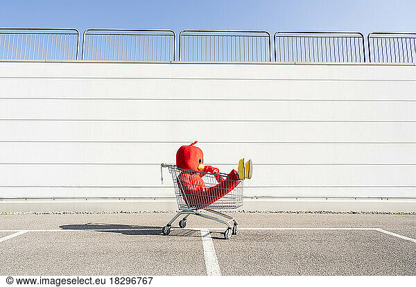 Woman wearing red duck costume sitting in shopping cart