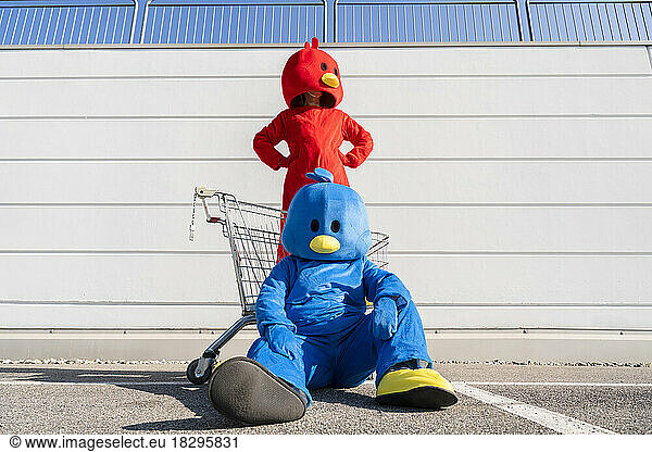 Woman wearing red duck costume standing in front of wall with man sitting on ground