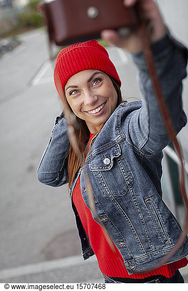Woman wearing red pullover  jeans jacket and wolly hat and taking a selfie