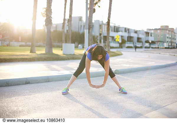 Woman wearing sports clothes hands together bending forwards stretching