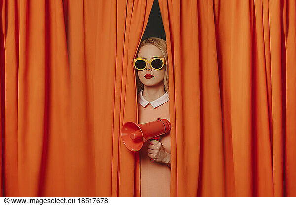 Woman wearing sunglasses standing with megaphone amidst curtains
