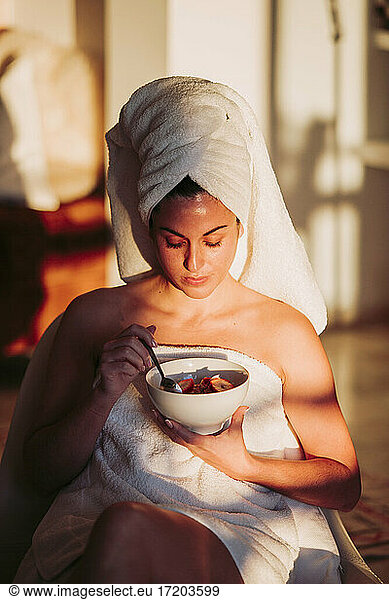 Woman wearing towel holding fruit bowl at home