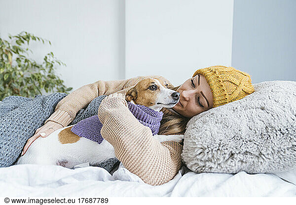 Woman wearing warm clothing cuddling with dog in bed