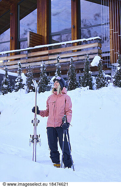 Woman wearing winter clothes holding skis in front of chalet