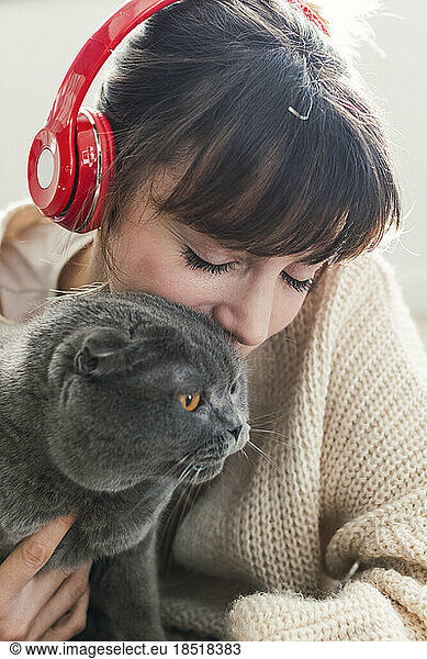 Woman wearing wireless headphones spending leisure time with cat