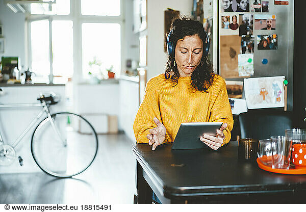 Woman wearing wireless headphones using tablet PC sitting at home