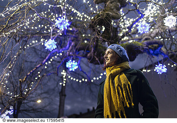 Woman wearing yellow scarf standing under illuminated tree