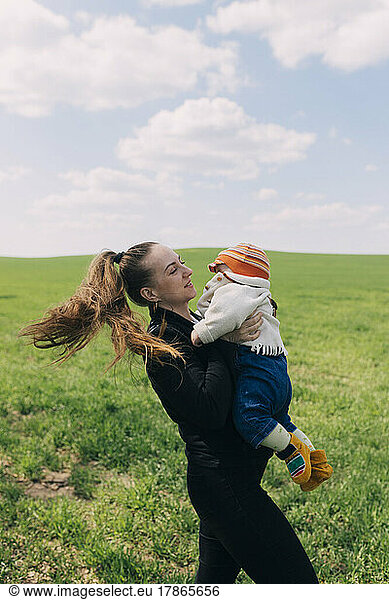 Woman with a baby in her arms standing on a green meadow
