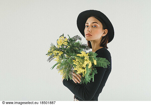 woman with a bouquet of mimosa and a hat on a white background