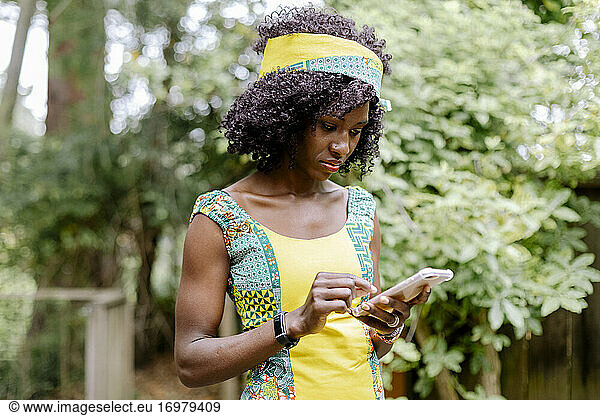 Woman with afro and head band using smart phone by garden