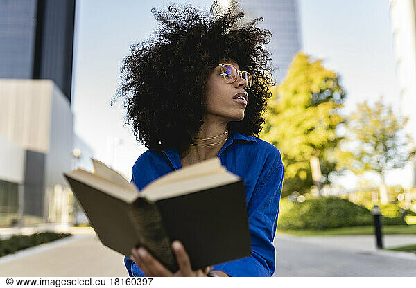 Woman with Afro hairstyle wearing eyeglasses holding book