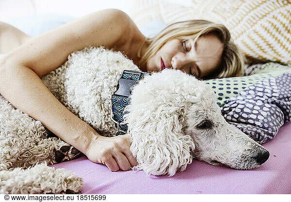 Woman with arm around dog sleeping in bed