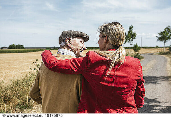 Woman with arm around senior man walking by field