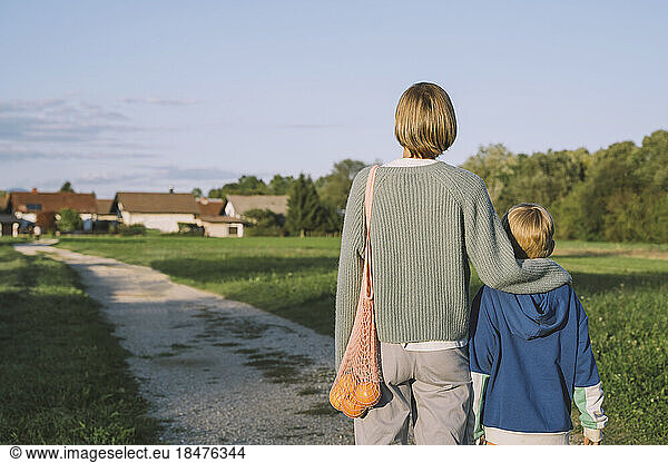 Woman with arm around son standing on footpath