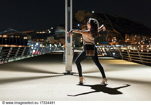Woman with arms outstretched dancing on pier at night