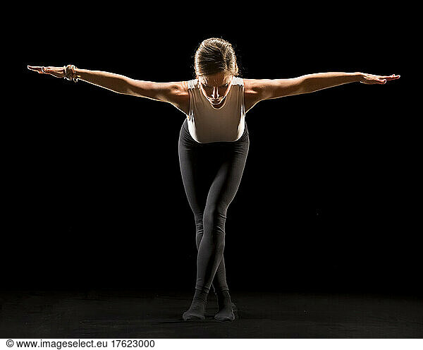 Woman with arms outstretched doing yoga against black background