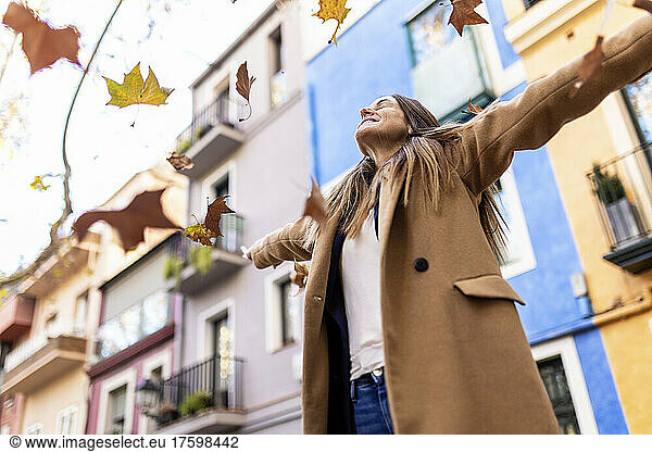 Woman with arms outstretched enjoying autumn leaves falling