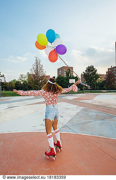 Woman with arms outstretched holding balloons roller skating at sports court