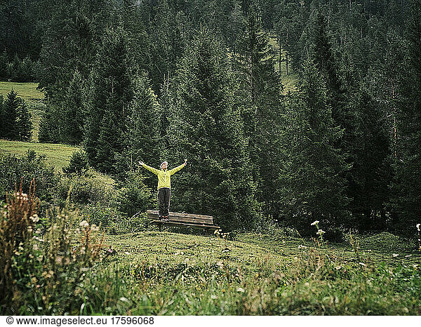 Woman with arms outstretched standing on bench in forest