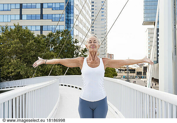 Woman with arms outstretched standing on footbridge