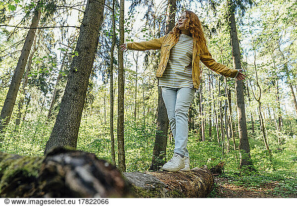 Woman with arms outstretched walking on fallen tree in forest