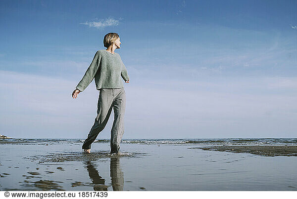Woman with arms outstretched walking on shore at beach