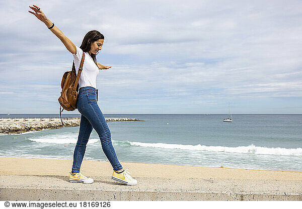 Woman with arms outstretched walking on wall